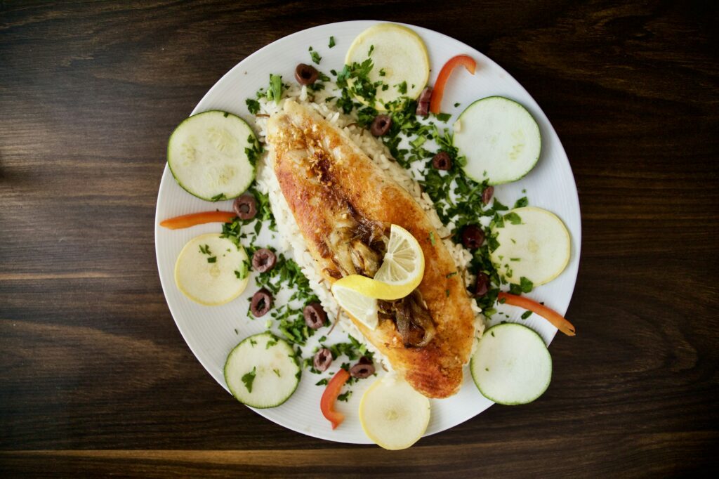 A plate of pan-fried Dalmatian fish with lemon, olives and parsley over rice on a dark wooden konoba table