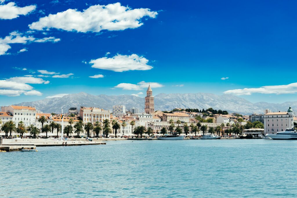 Split's palm-lined Riva waterfront promenade with the cathedral bell tower and boats — the walkable, car-free heart of the city