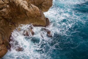 Wind-driven white surf breaking against ochre limestone rocks in turquoise Adriatic water