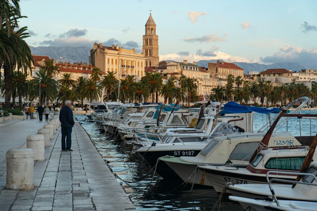 The Riva promenade in Split at golden hour with palms, the cathedral bell tower and moored boats